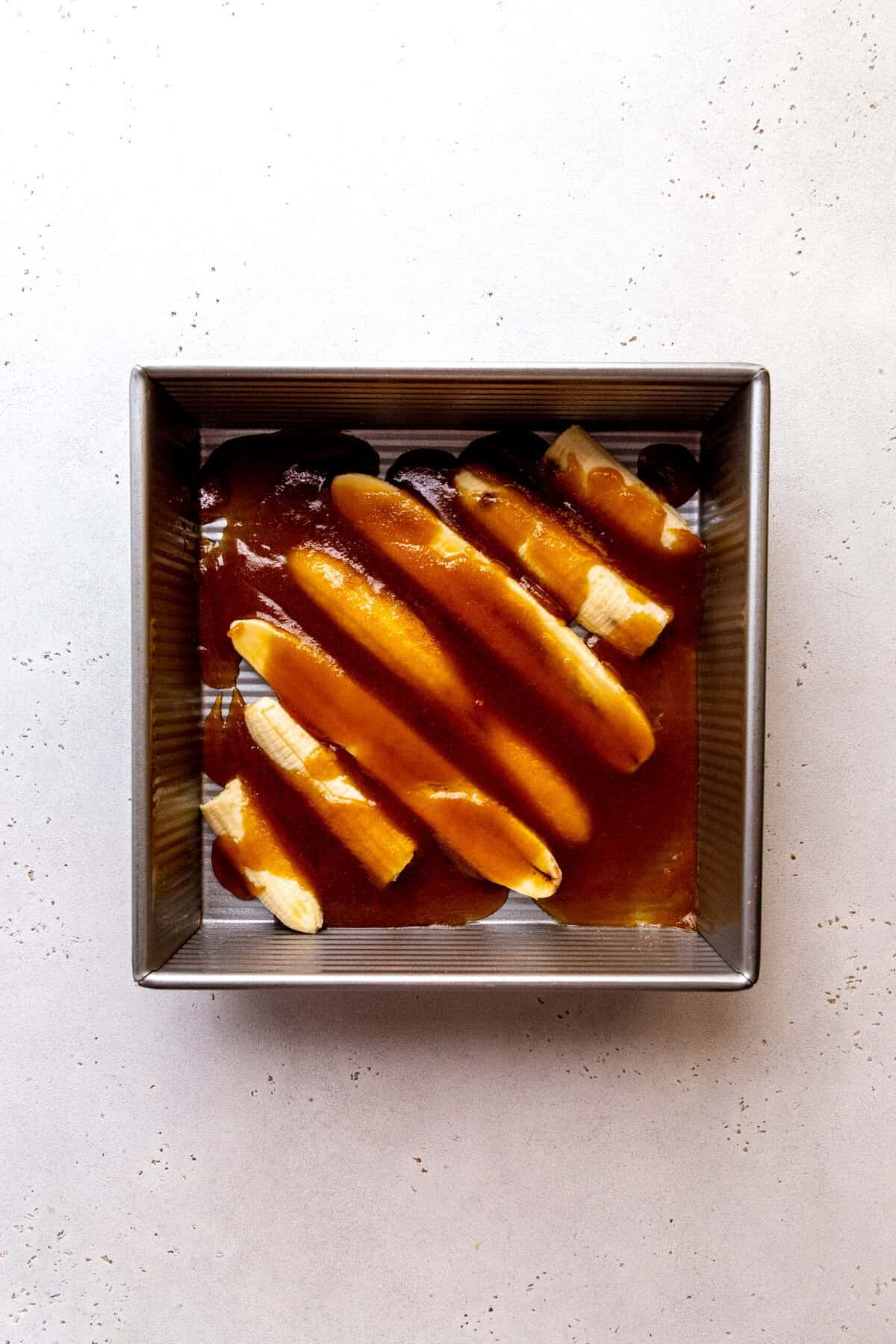 Sliced bananas covered in caramel sauce in a square pan.