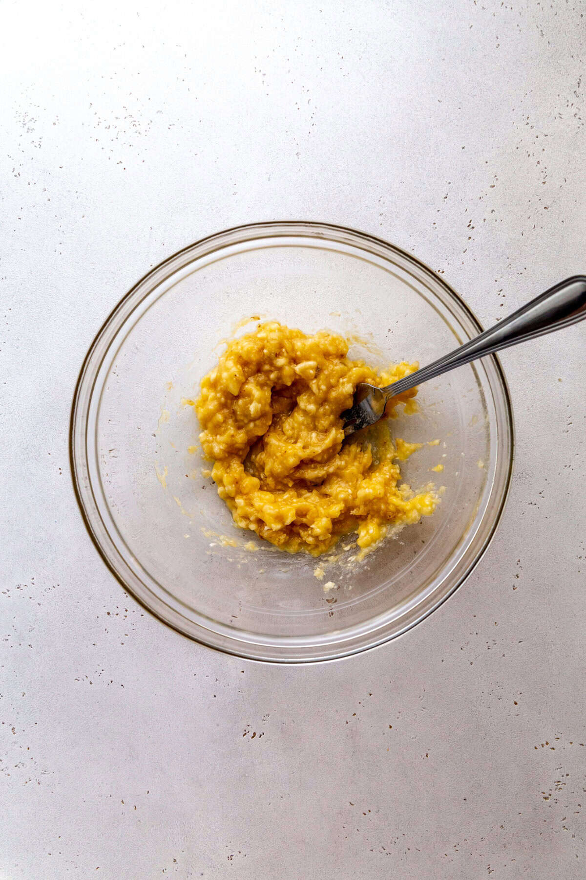 Glass bowl filled with mashed bananas and a fork.