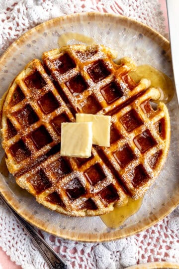 Belgian waffle topped with butter and syrup on a plate with a fork and knife.