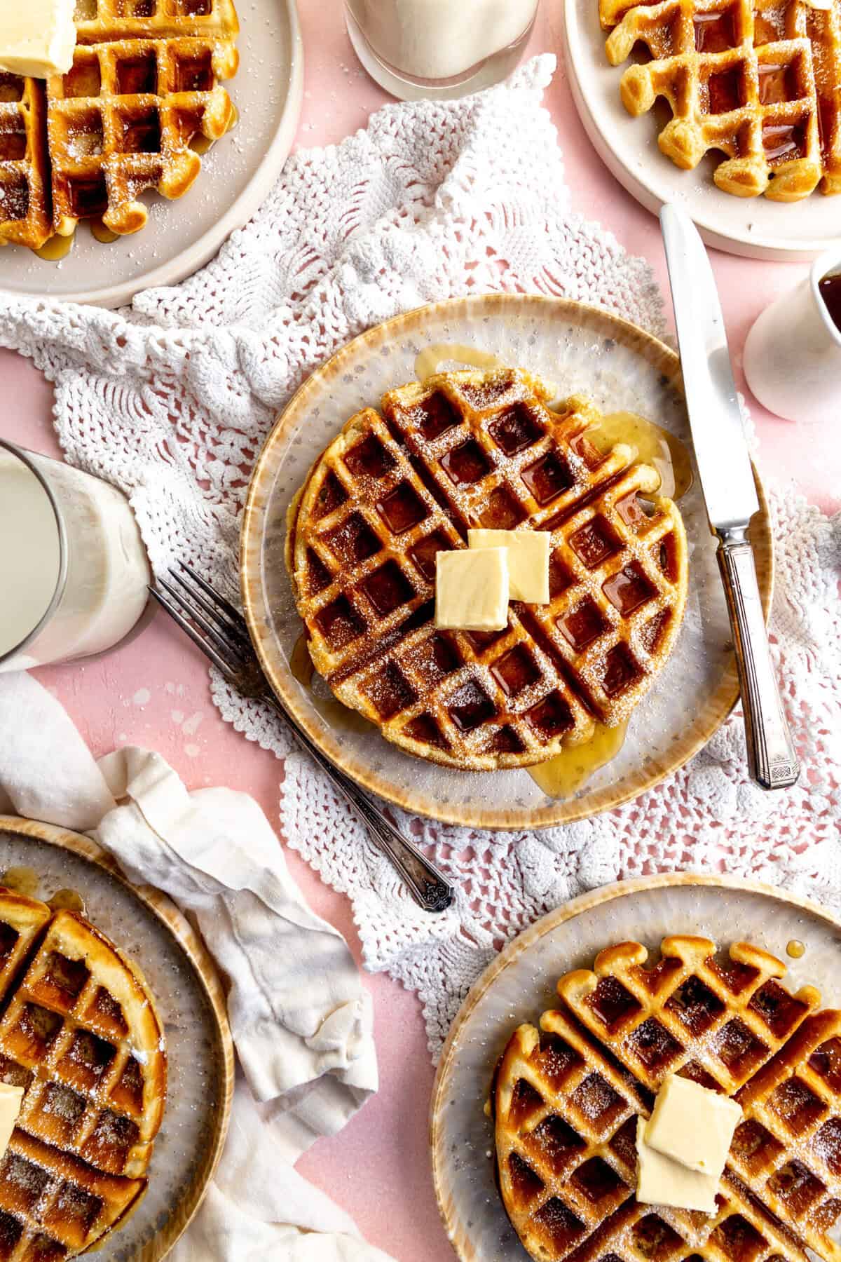 Vegan Belgian waffles topped with butter and maple syrup and glasses of milk.