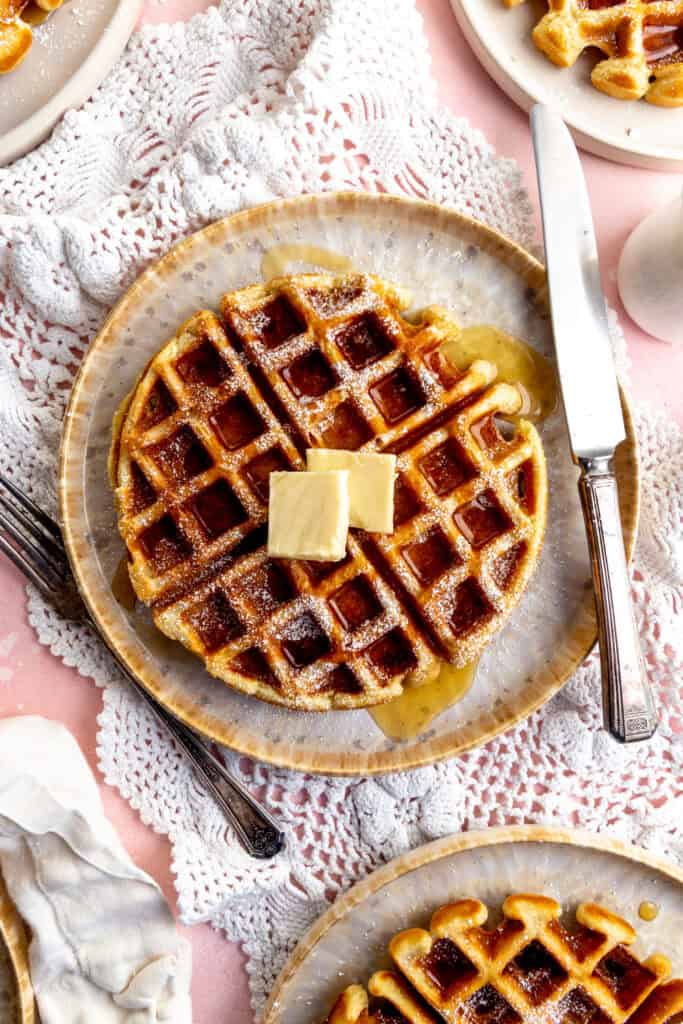 Knife cutting into a Belgian waffle topped with butter and maple syrup.