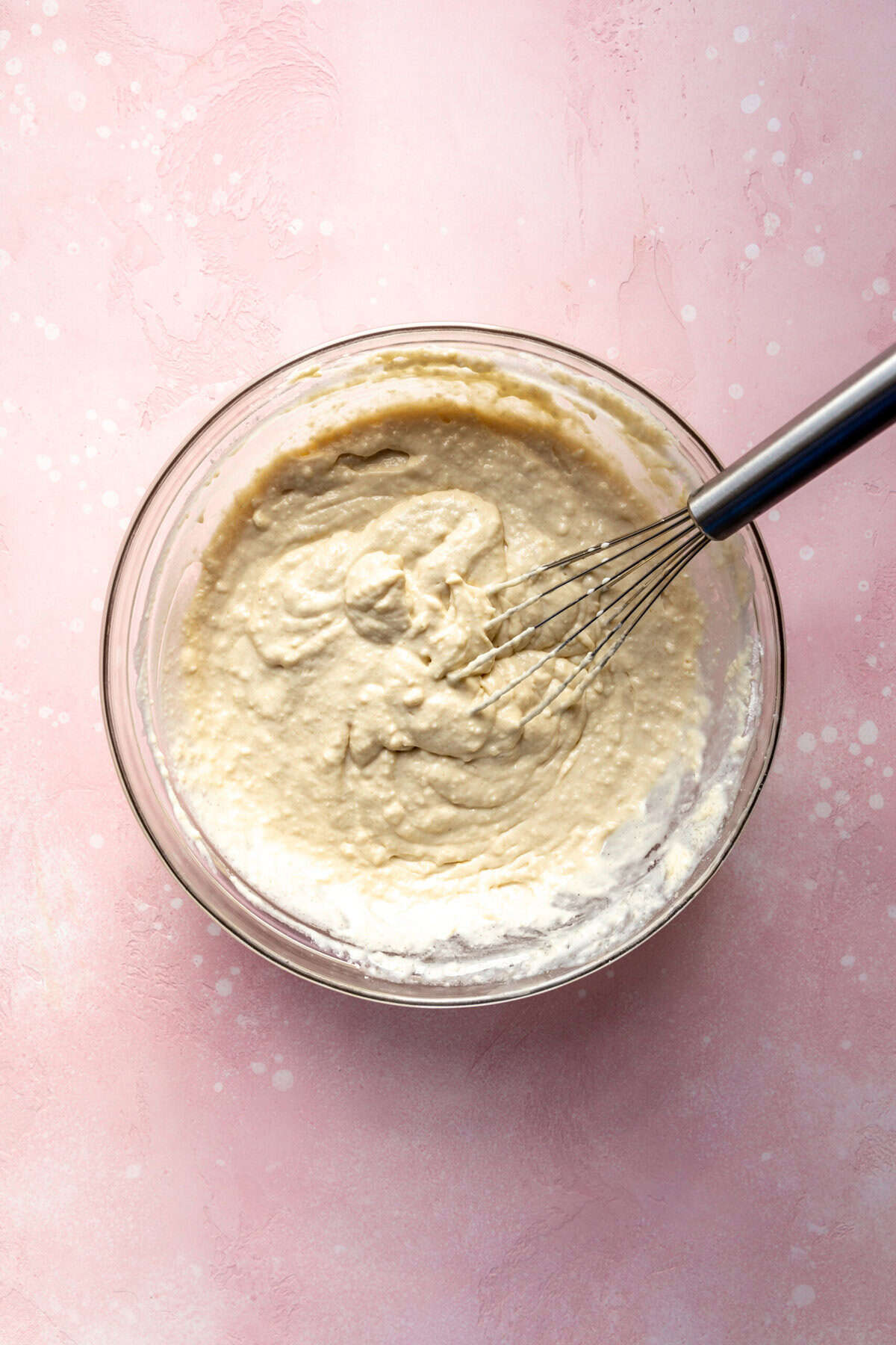 Glass bowl of waffle batter and a wire whisk.