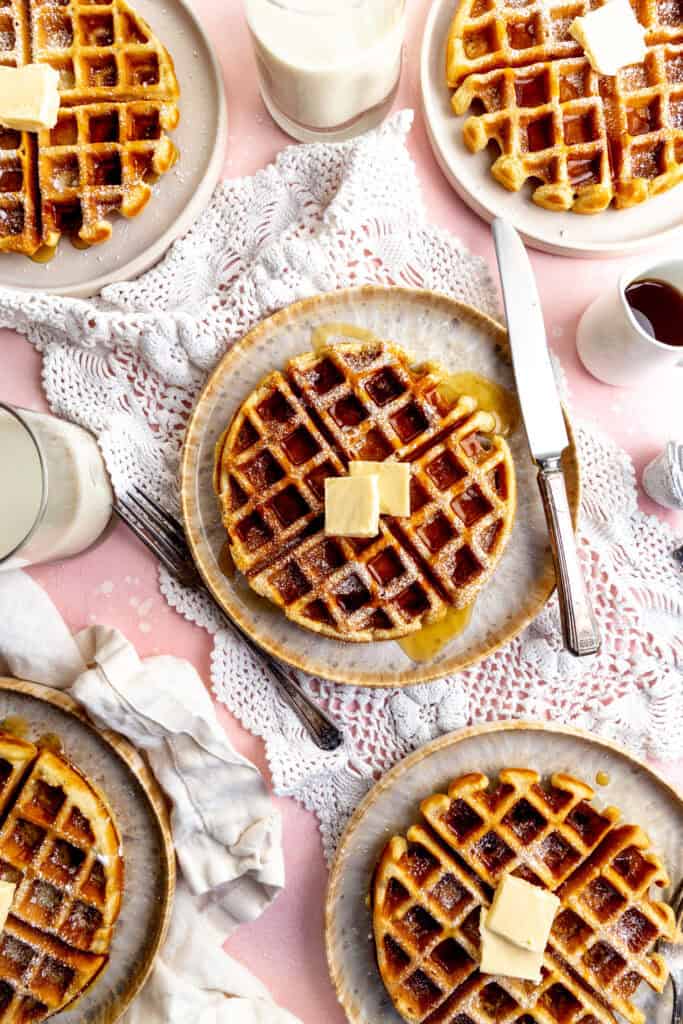 Waffles on plates with forks and knives, and a cup of milk.