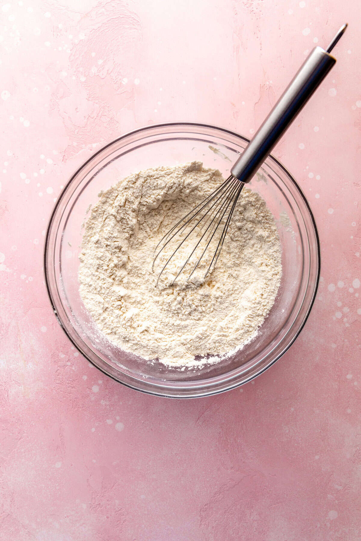 Glass bowl of flour and a wire whisk.