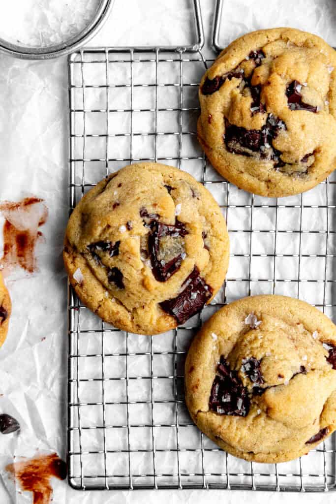 Vegan chocolate chip cookies on a wire rack and a cup of flaky salt.