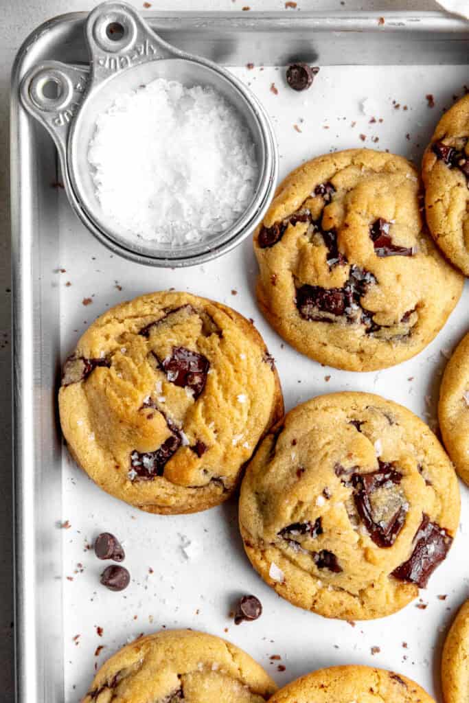 Chocolate chip cookies on a baking sheet and a cup of flaky salt.