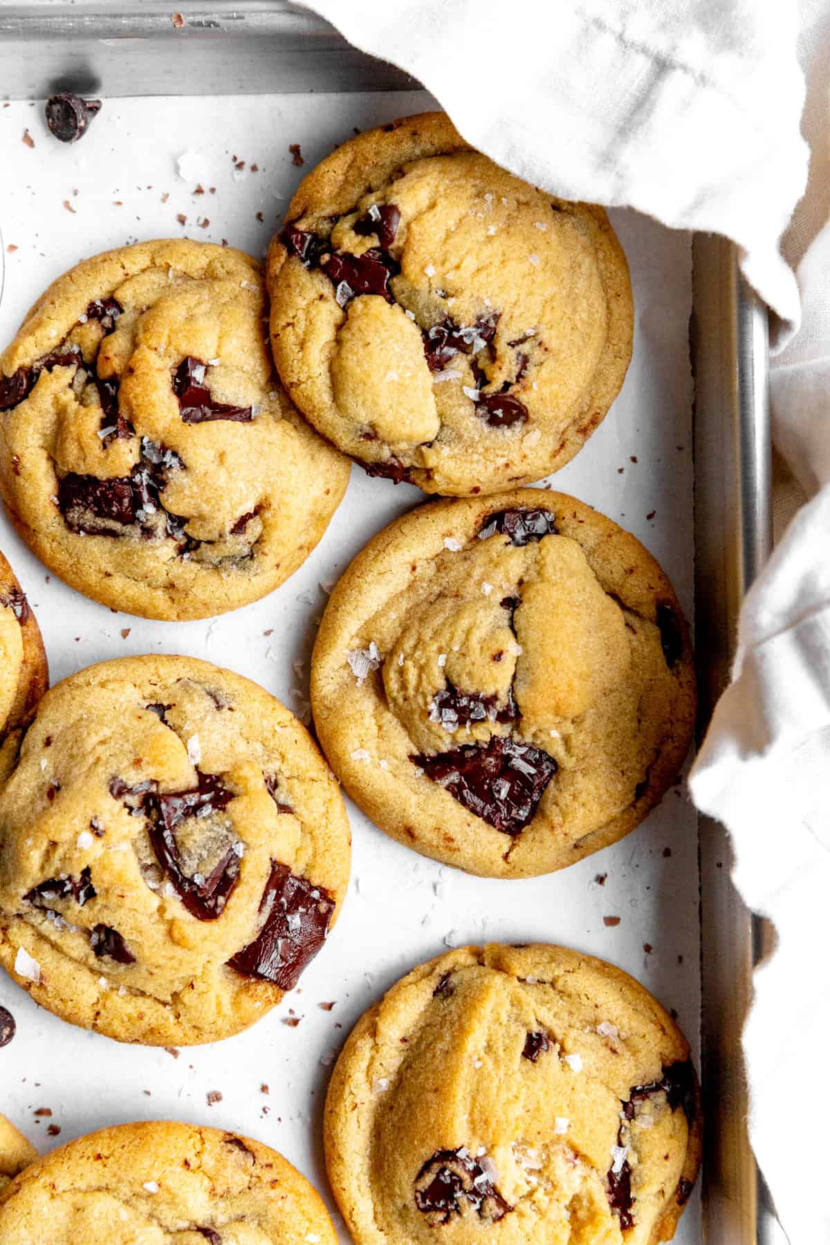 Chocolate chip cookies topped with flaky salt on a baking sheet with a linen napkin.
