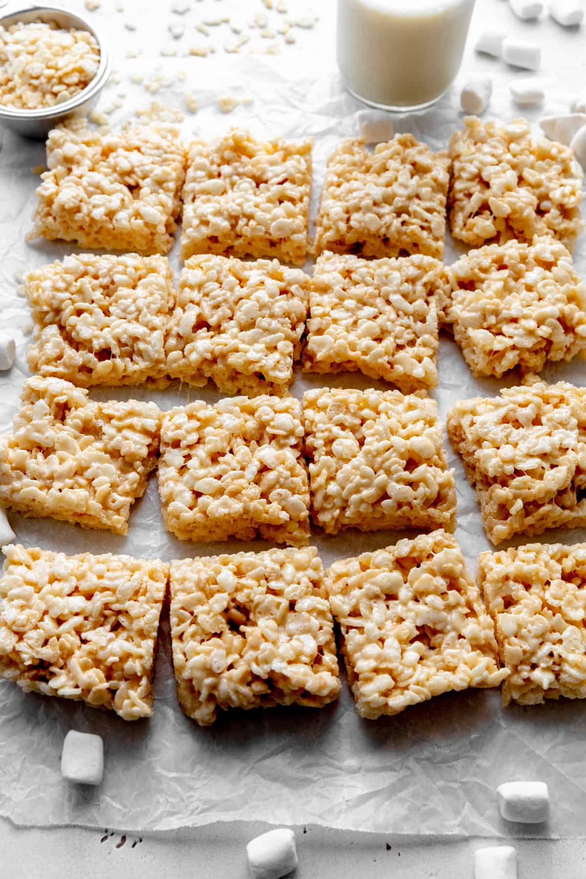 Rice krispie treats, scattered marshmallows and a glass of milk.