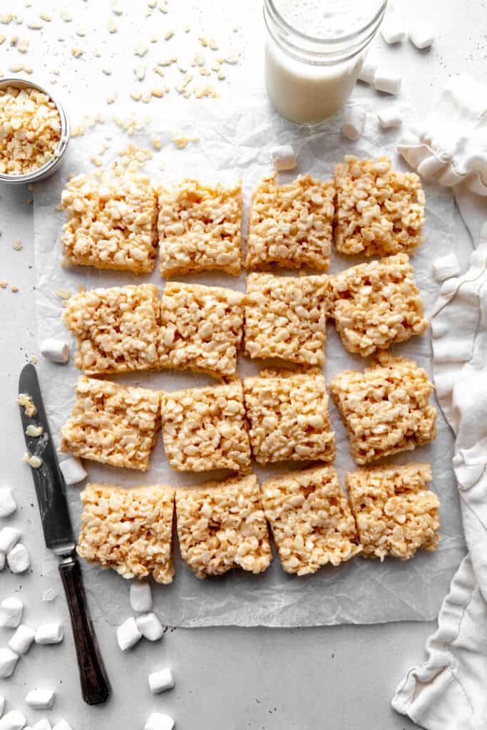 Vegan rice krispie treats cut into squares, a cup of milk and a linen napkin.