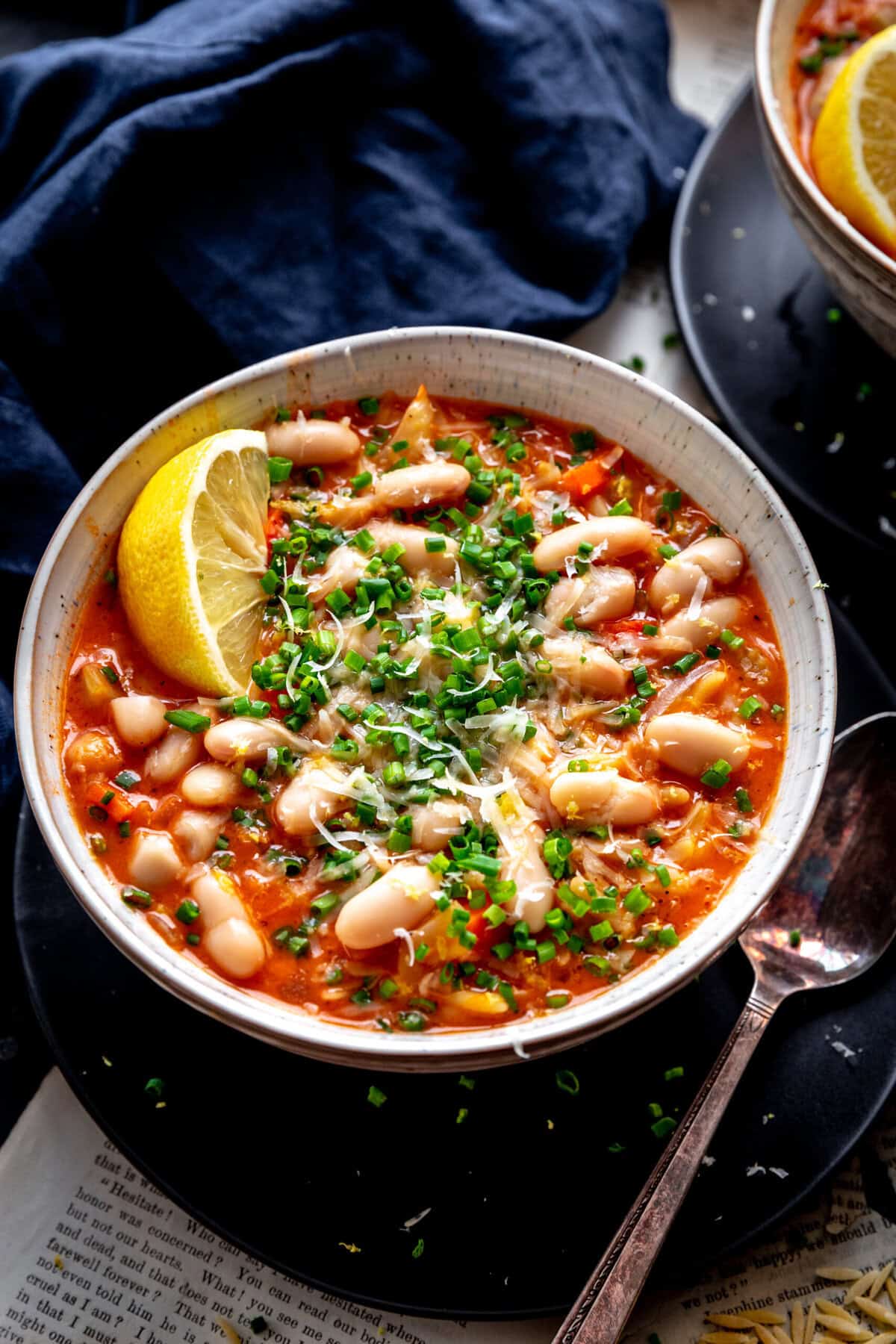 Bowl of tomato orzo soup, a lemon wedge and a spoon.