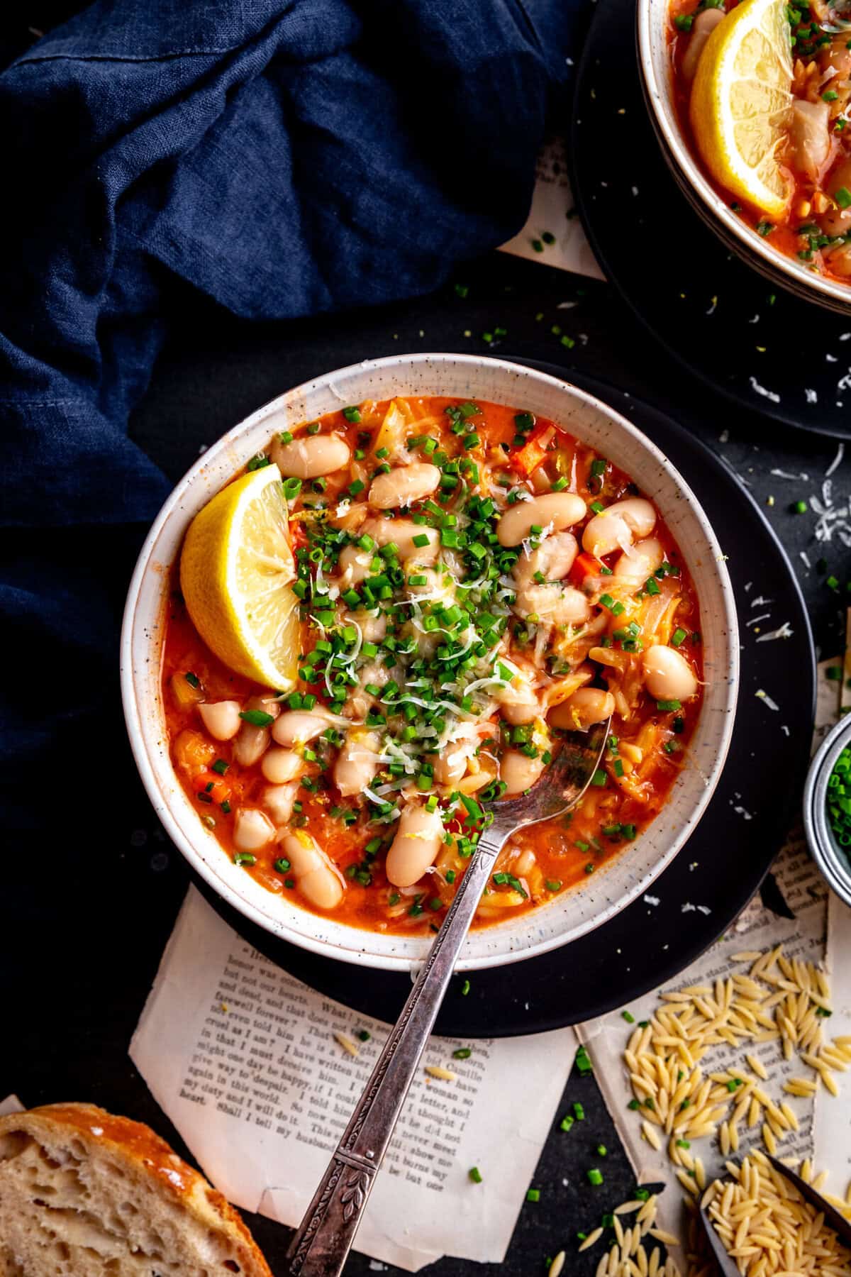 Spoon digging into a bowl of vegetable orzo tomato soup and a navy napkin.