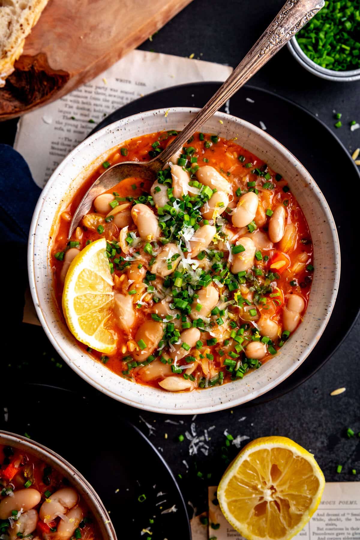 Spoon stuck in a bowl of orzo tomato soup topped with chives and parmesan.