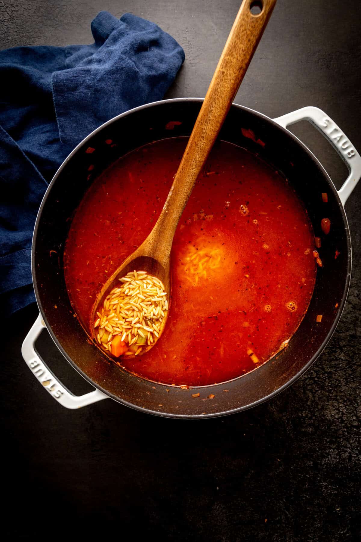 Tomato soup in a large pot with uncooked orzo.