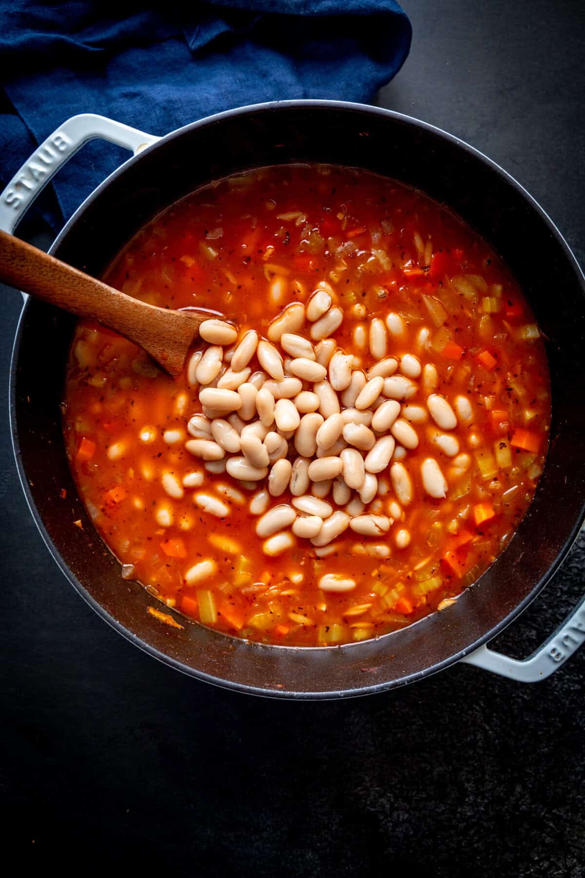 White beans poured into a pot of vegetable soup.