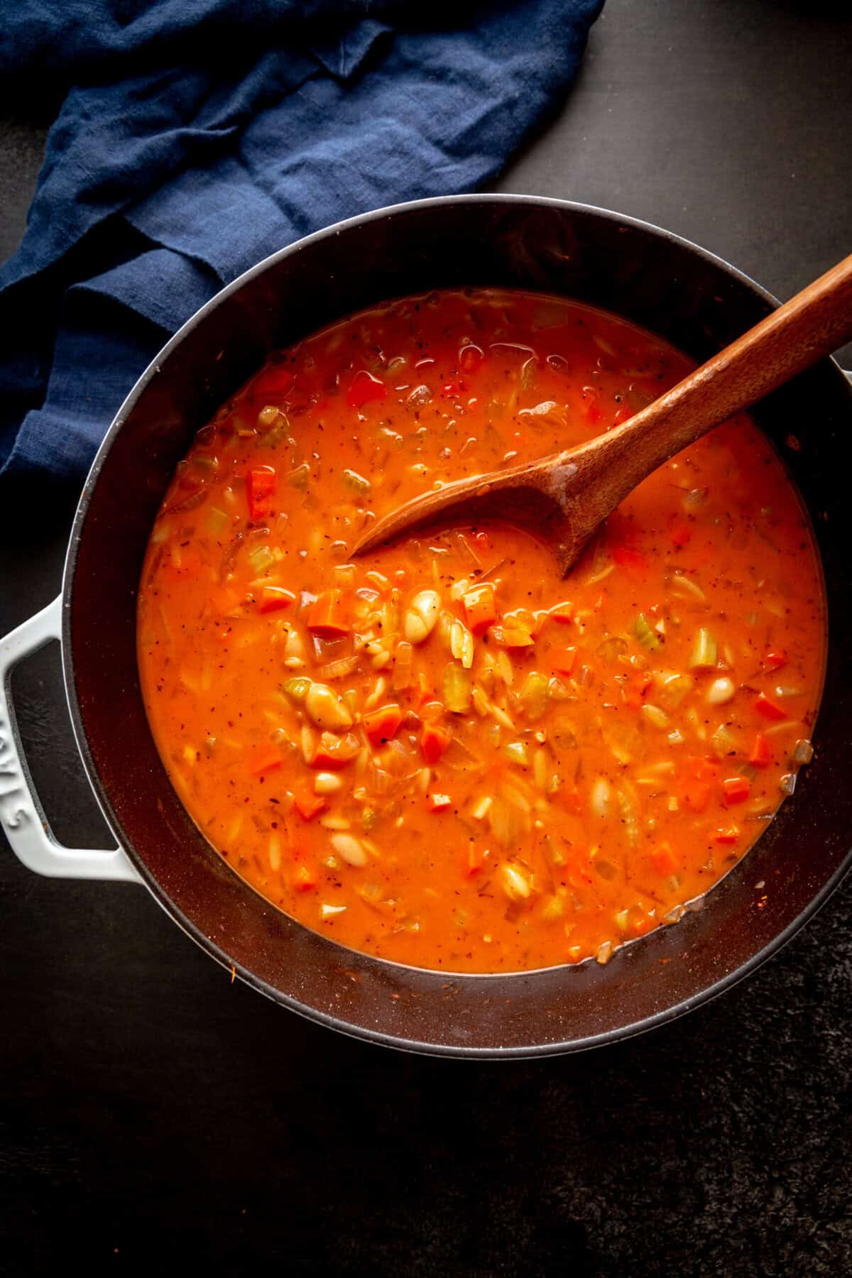 Vegetable orzo tomato soup in a large pot with a wooden spoon.