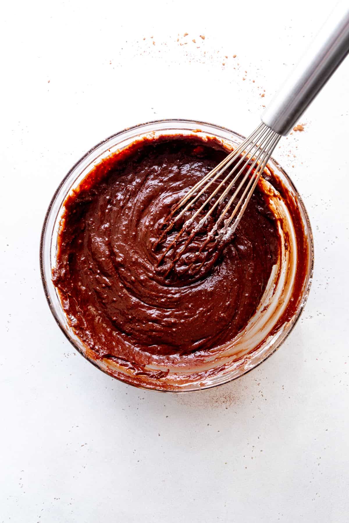Brownie batter in a glass bowl with a whisk.