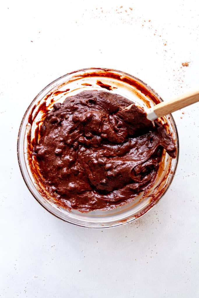 Brownie batter with chocolate chips in a glass bowl with a rubber spatula.
