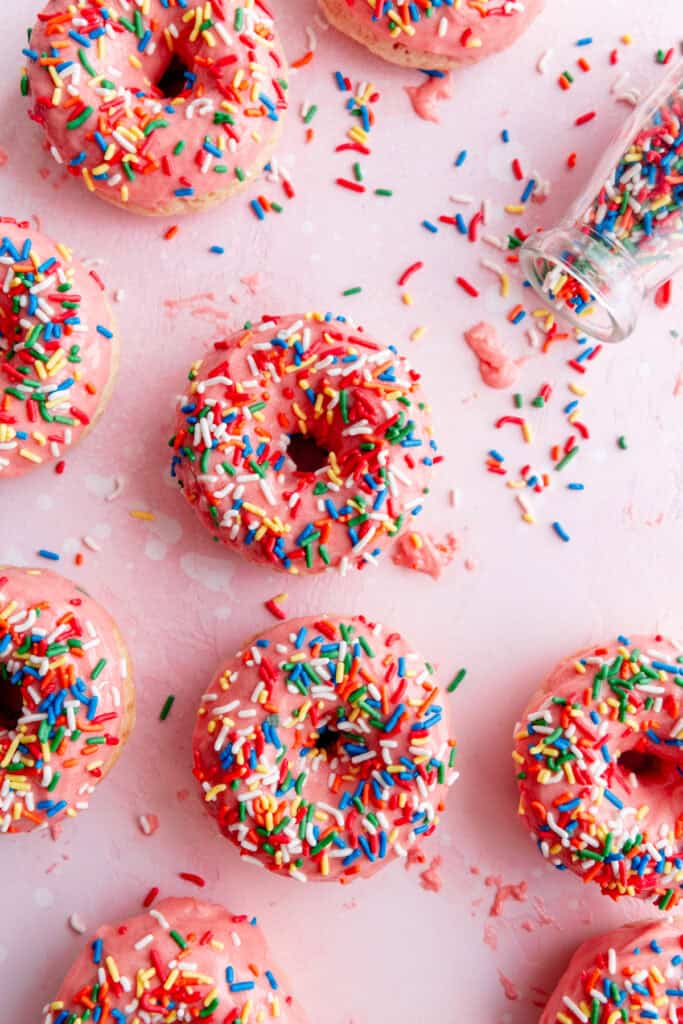 Rainbow sprinkles spilling out of a jar and pink sprinkle donuts.