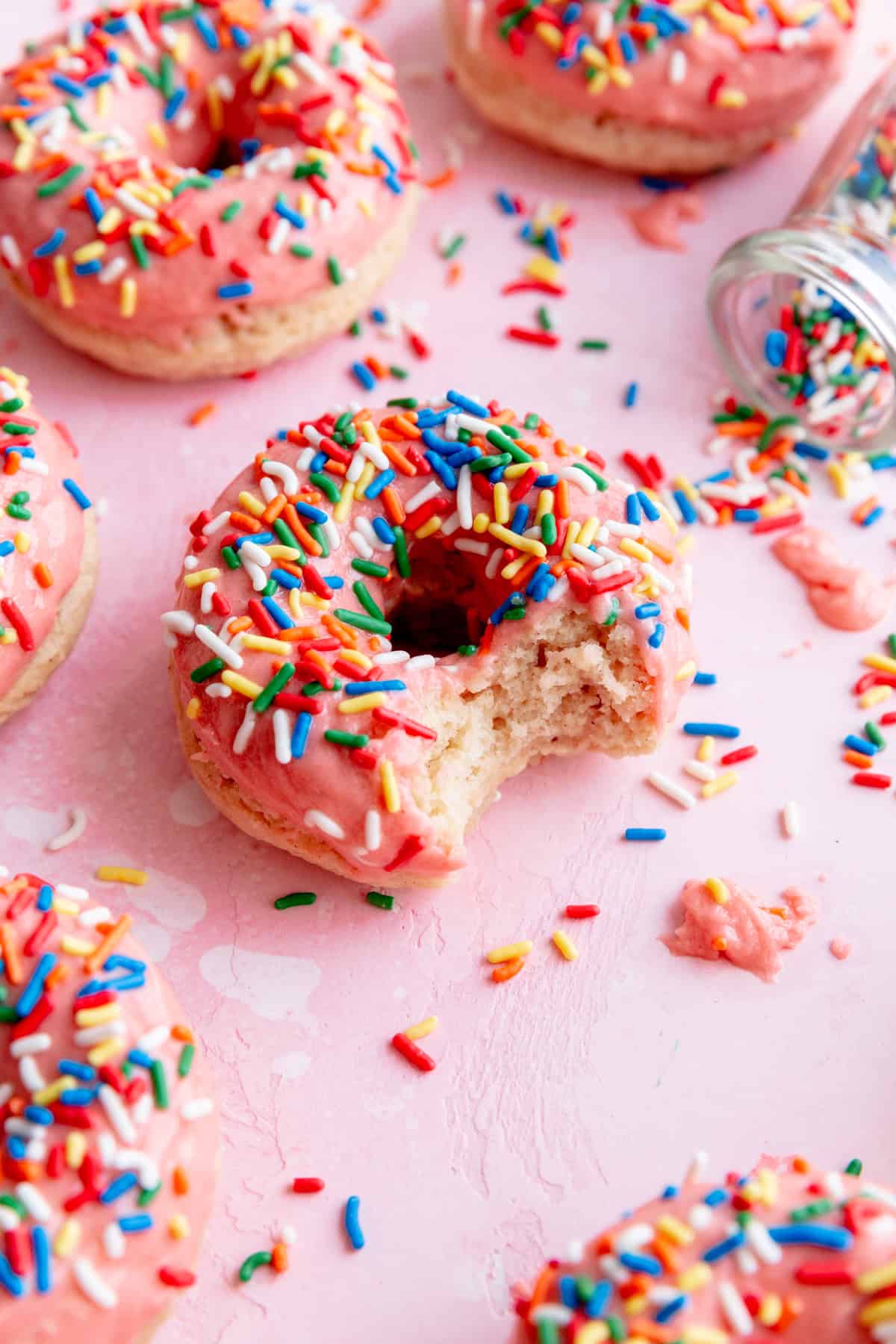 Baked donut topped with pink icing and sprinkles with a bite taken out of it.