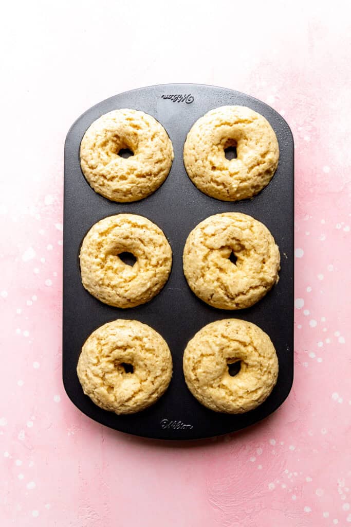 Baked donuts in a donut pan on a pink surface.