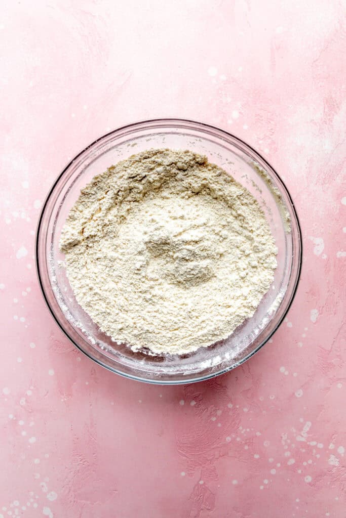 Flour in a glass bowl on a pink surface.