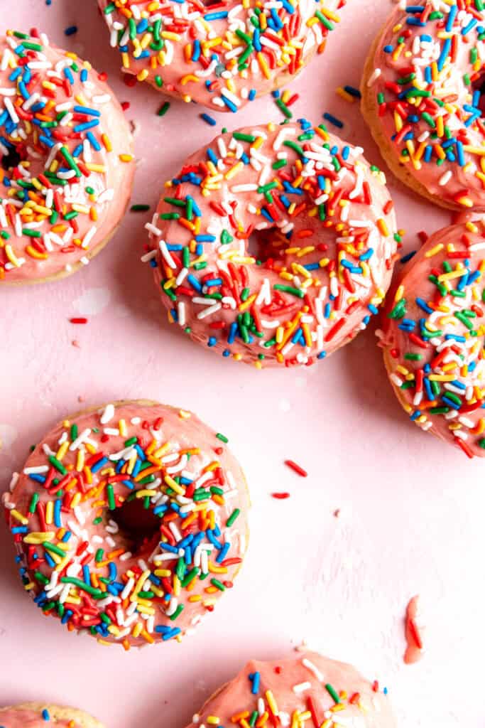 Pink sprinkle donuts on a pink surface.