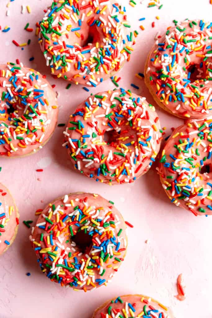 Baked donuts topped with strawberry icing and rainbow sprinkles.