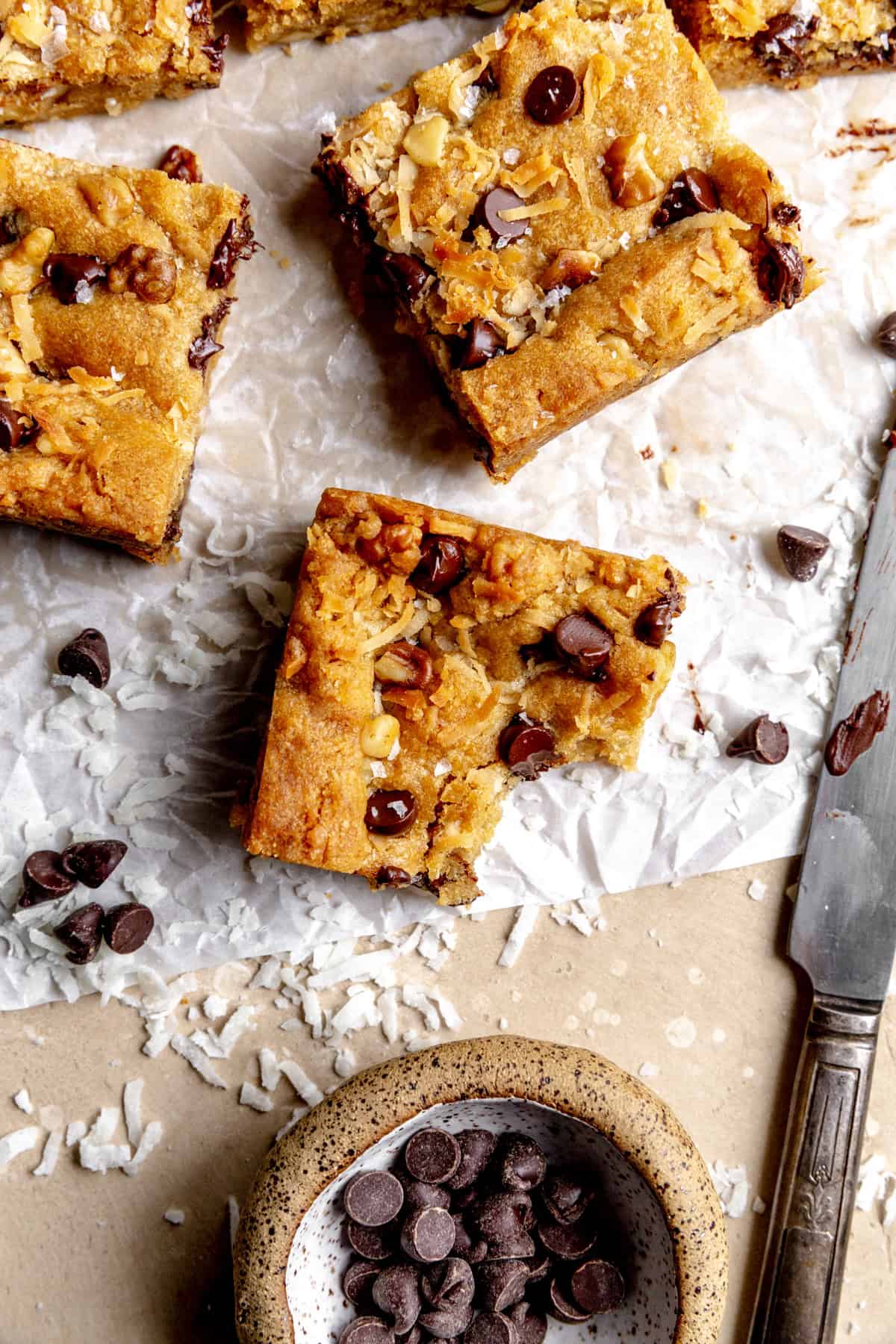 Vegan blondie with a bite taken out of it and a cup of chocolate chips.