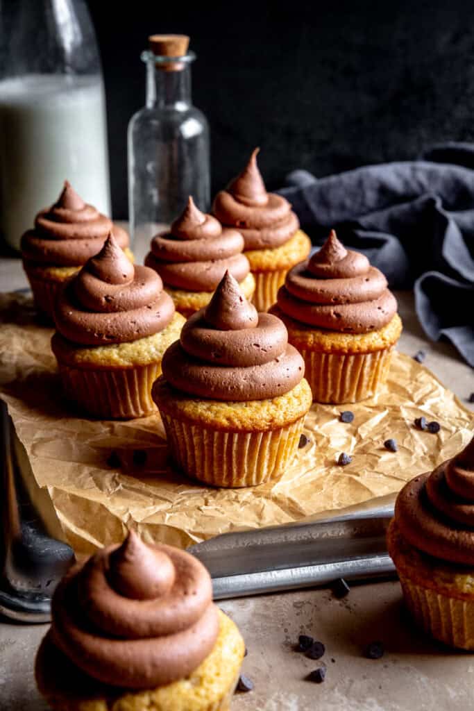 Cupcakes with chocolate frosting on a baking sheet and a jug of milk.