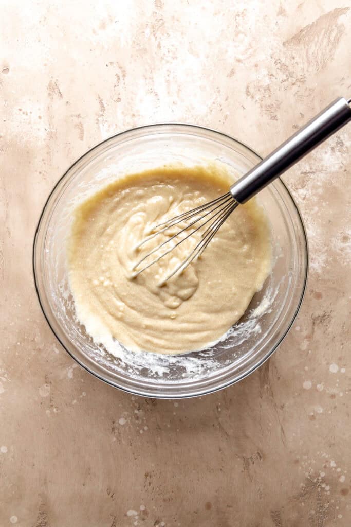 Vanilla cake batter in a glass bowl with a wire whisk.