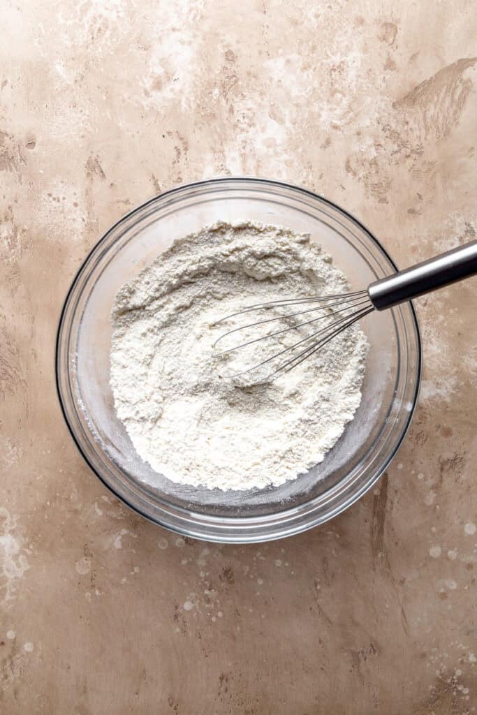 Flour and a wire whisk in a glass bowl.