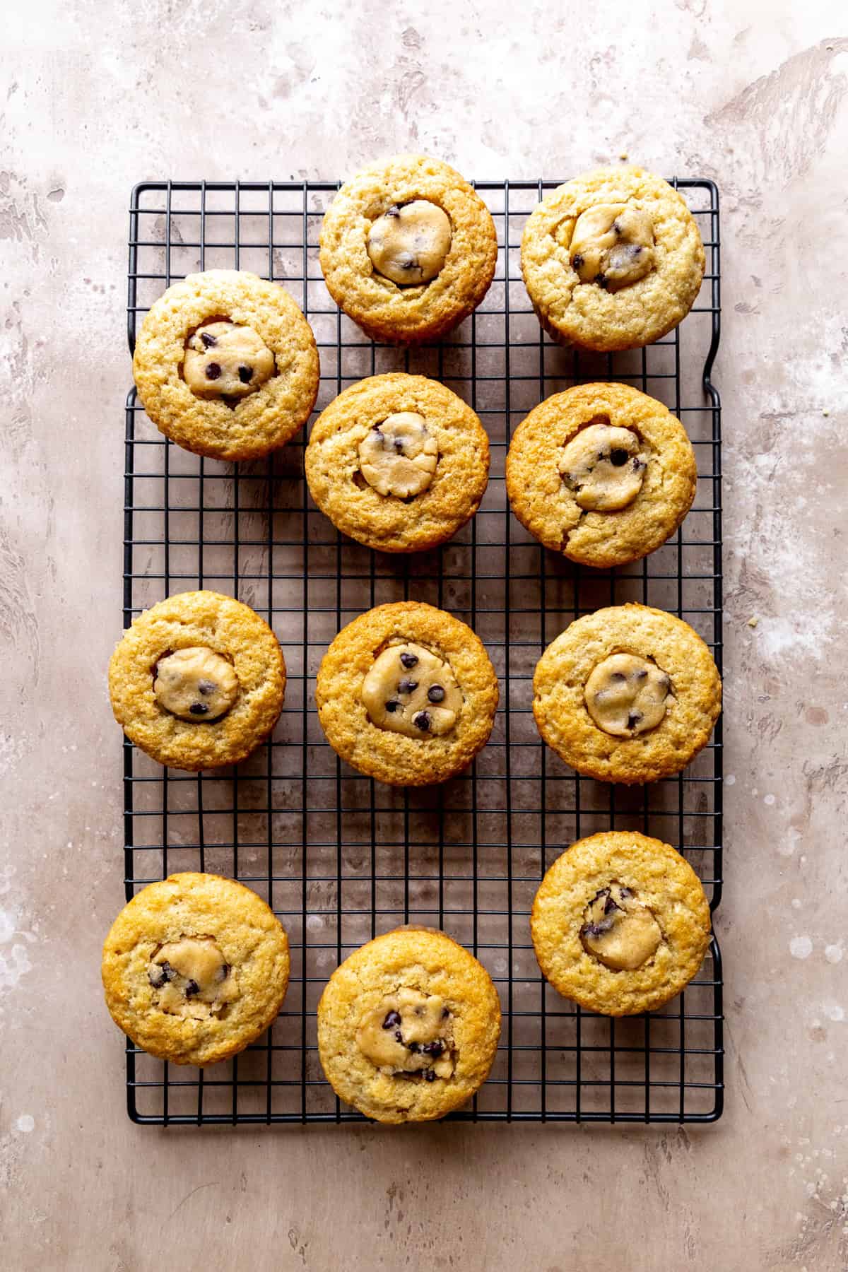 Vanilla cupcakes stuffed with chocolate chip cookie dough on a wire cooling rack.