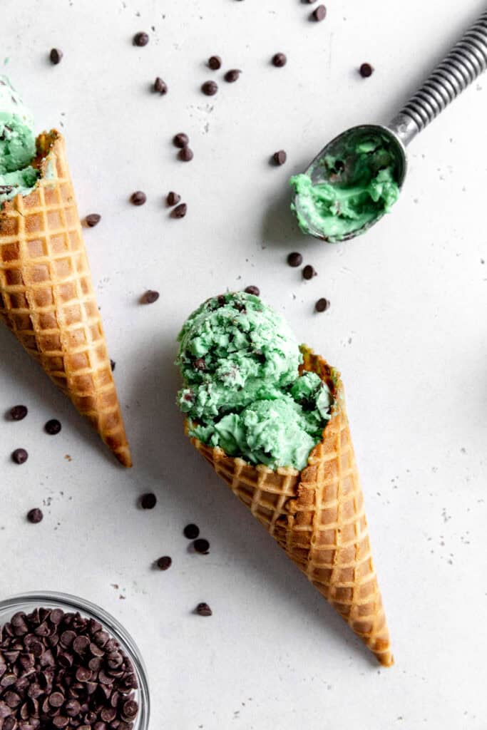 Two waffle cones of mint chip ice cream and a metal ice cream scoop.