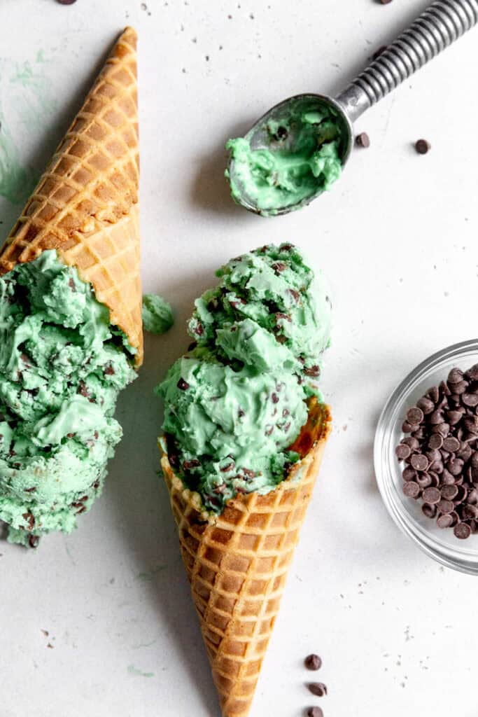 Two waffle cones of mint chip ice cream and a metal ice cream scoop.