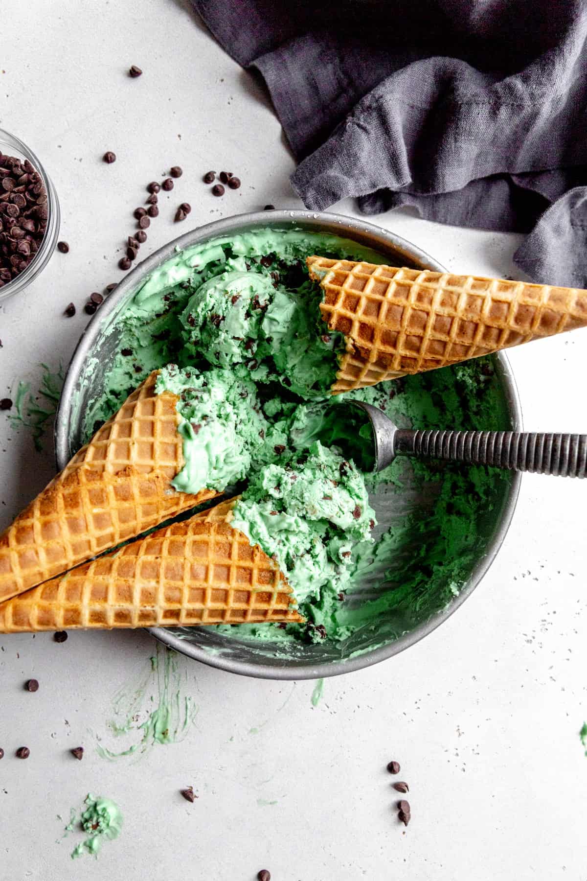 Waffle cones face down in a pan of mint chip ice cream.