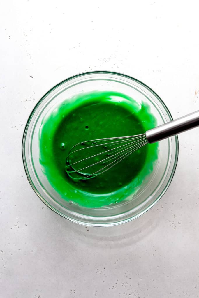 Glass bowl of green sweetened condensed milk and a whisk.