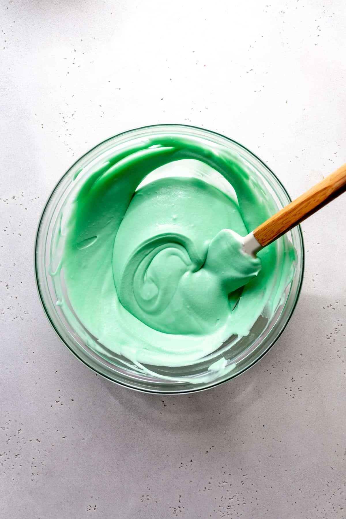 Glass bowl of green whipped cream and a rubber spatula.