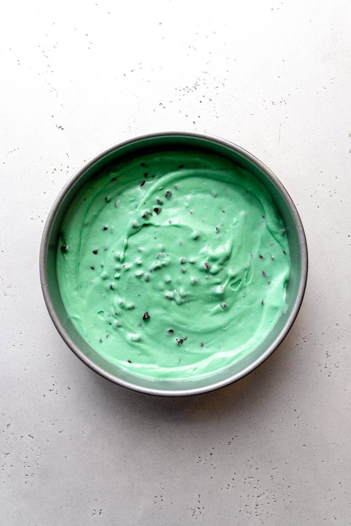 Unfrozen mint chip ice cream base in a round cake pan.