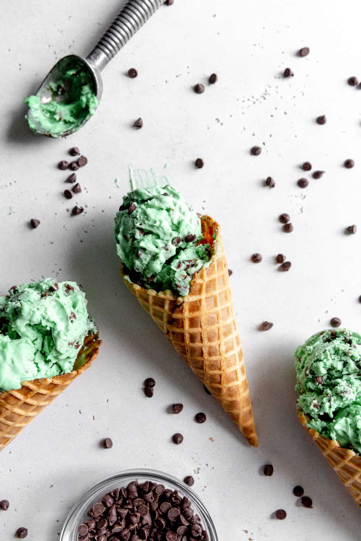 Three waffle cones with mint chip ice cream and a bowl of mini chocolate chips.