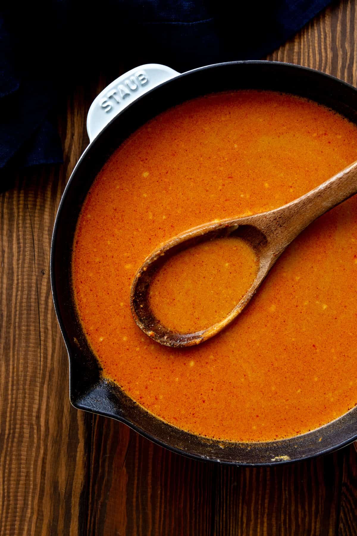 Ramen broth in a white skillet with a wooden spoon.