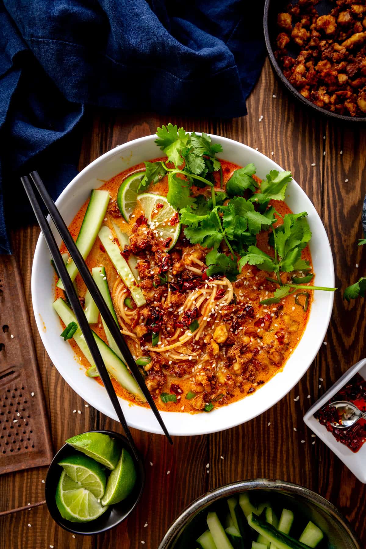 Bowl of miso curry ramen topped with cilantro, cucumber and lime wedges with chopsticks.