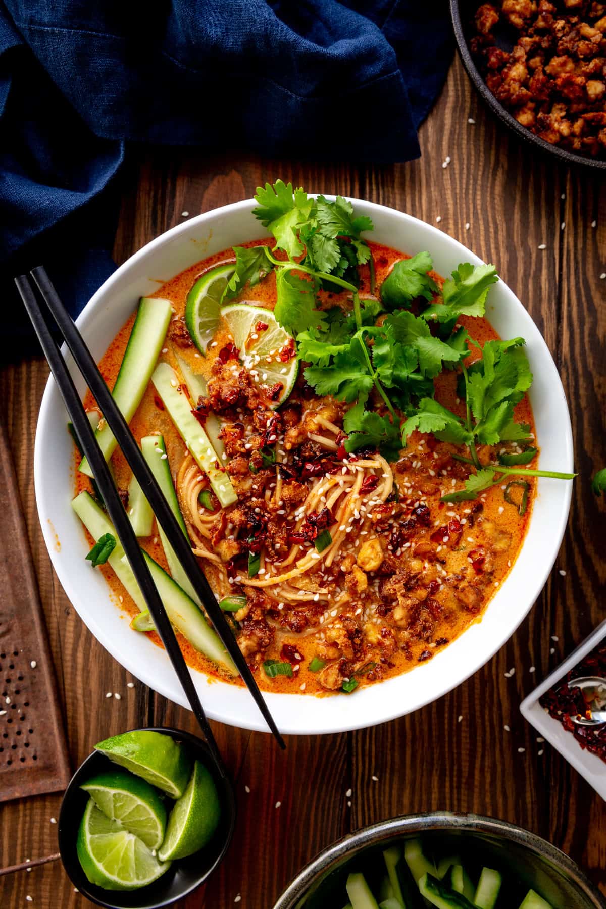 Bowl of miso curry ramen topped with cilantro, cucumber and lime wedges with a linen napkin.