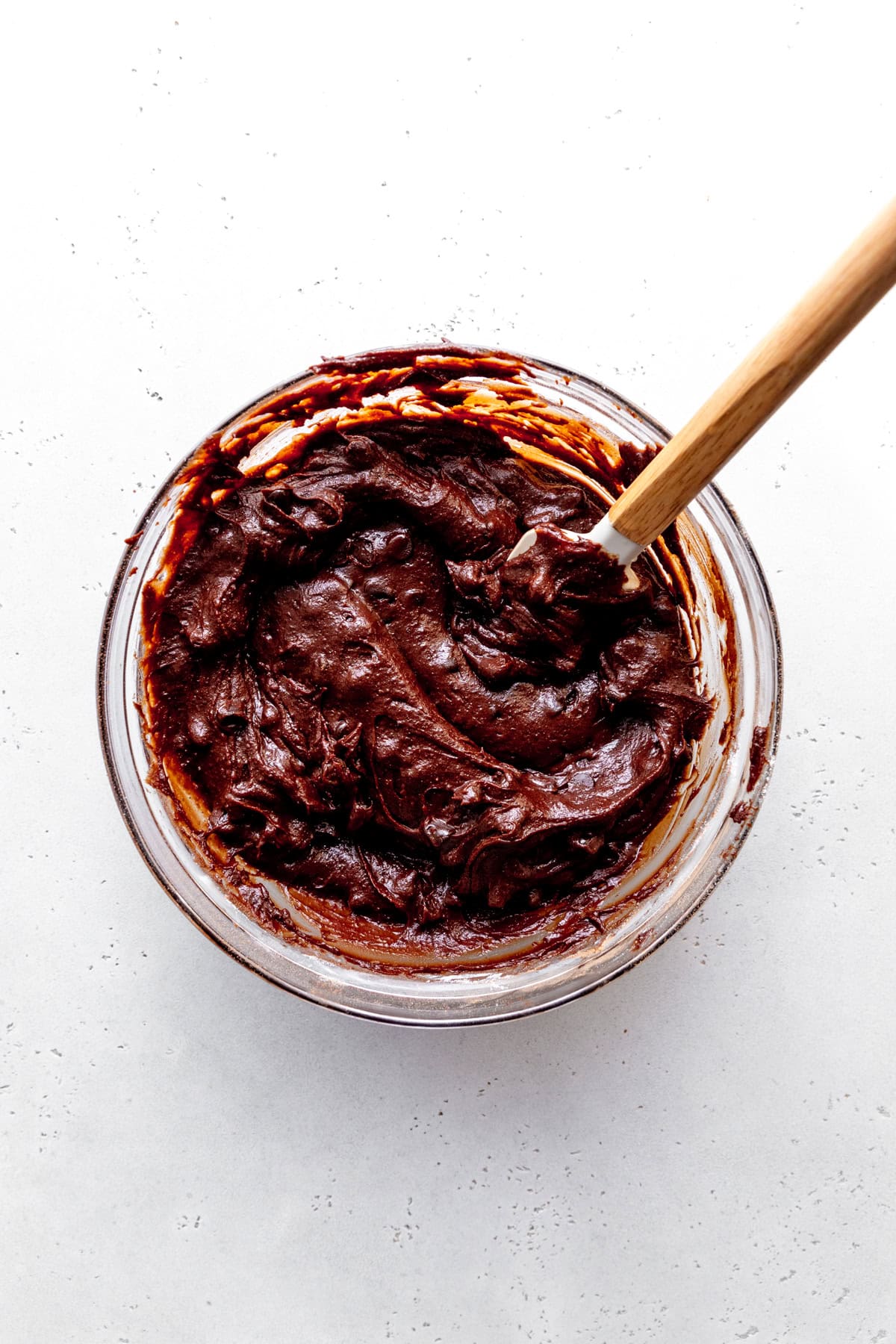 Brownie batter in a glass bowl with a rubber spatula.