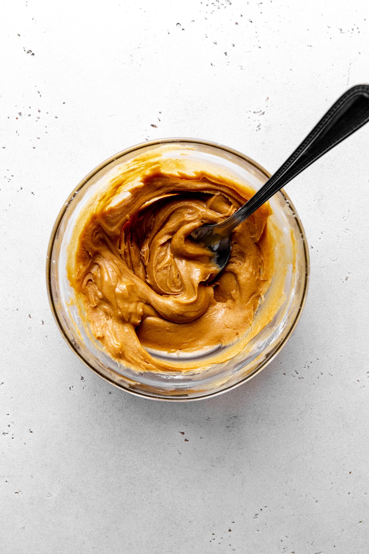 Peanut butter in a glass bowl with a spoon.