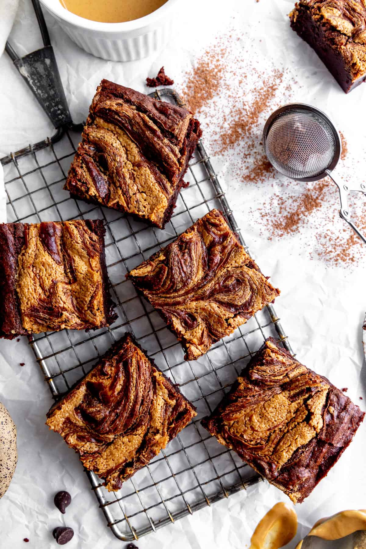 Peanut butter brownies on a wire cooling rack and a cup of peanut butter.