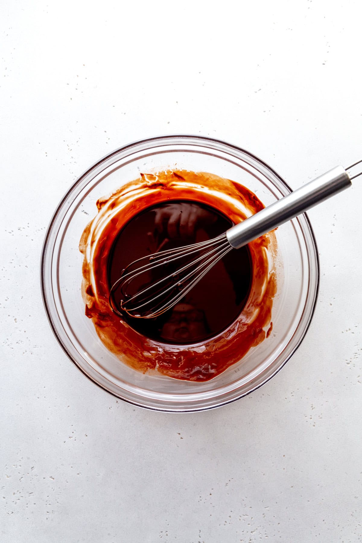 Glass bowl of melted chocolate and a wire whisk.