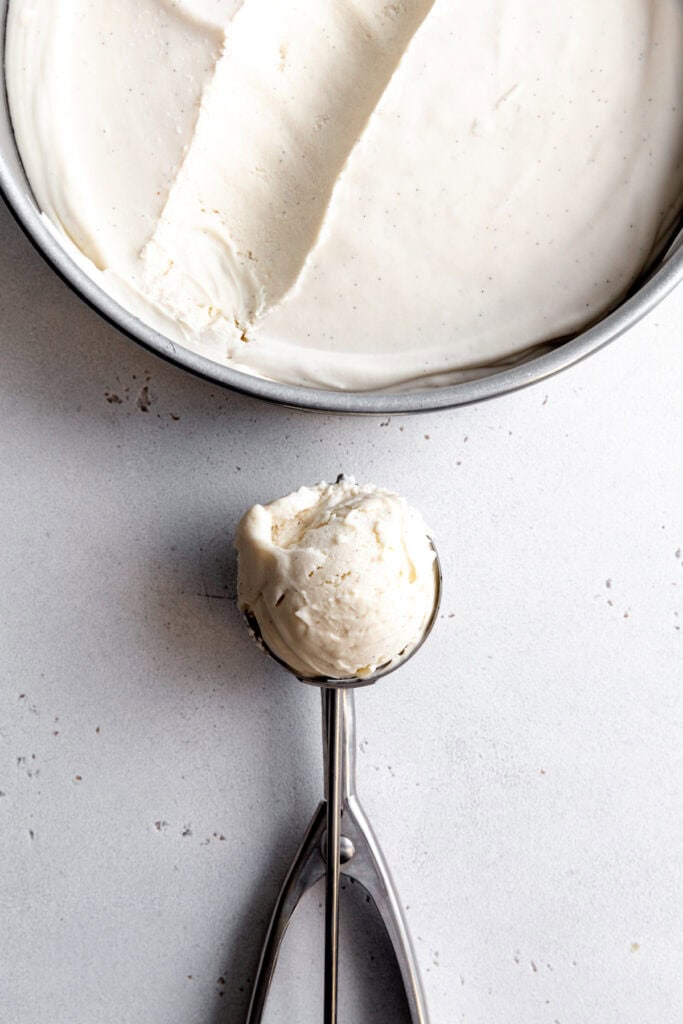 Ice cream scoop full of vanilla ice cream and ice cream in a round pan.