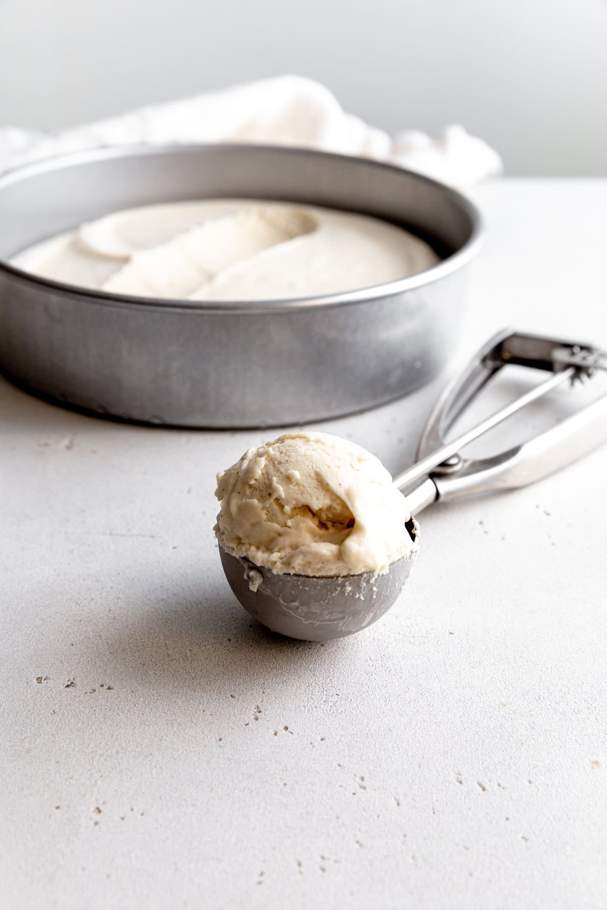 Ice cream scoop full of vanilla ice cream and a round pan of ice cream.