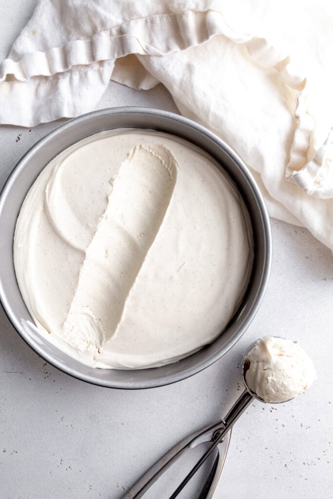 Cake pan of vanilla ice cream and an ice cream scoop full of ice cream.