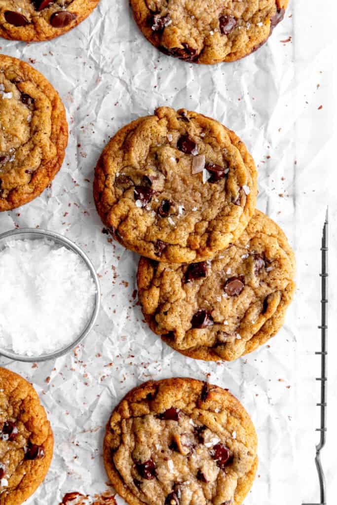 Banana chocolate chip cookies on a wire rack with a cup of flaky salt.